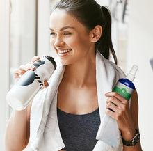 Woman holding Pristine Body Cleansing Spray bottle in one hand and a water bottle in the other hand after a workout